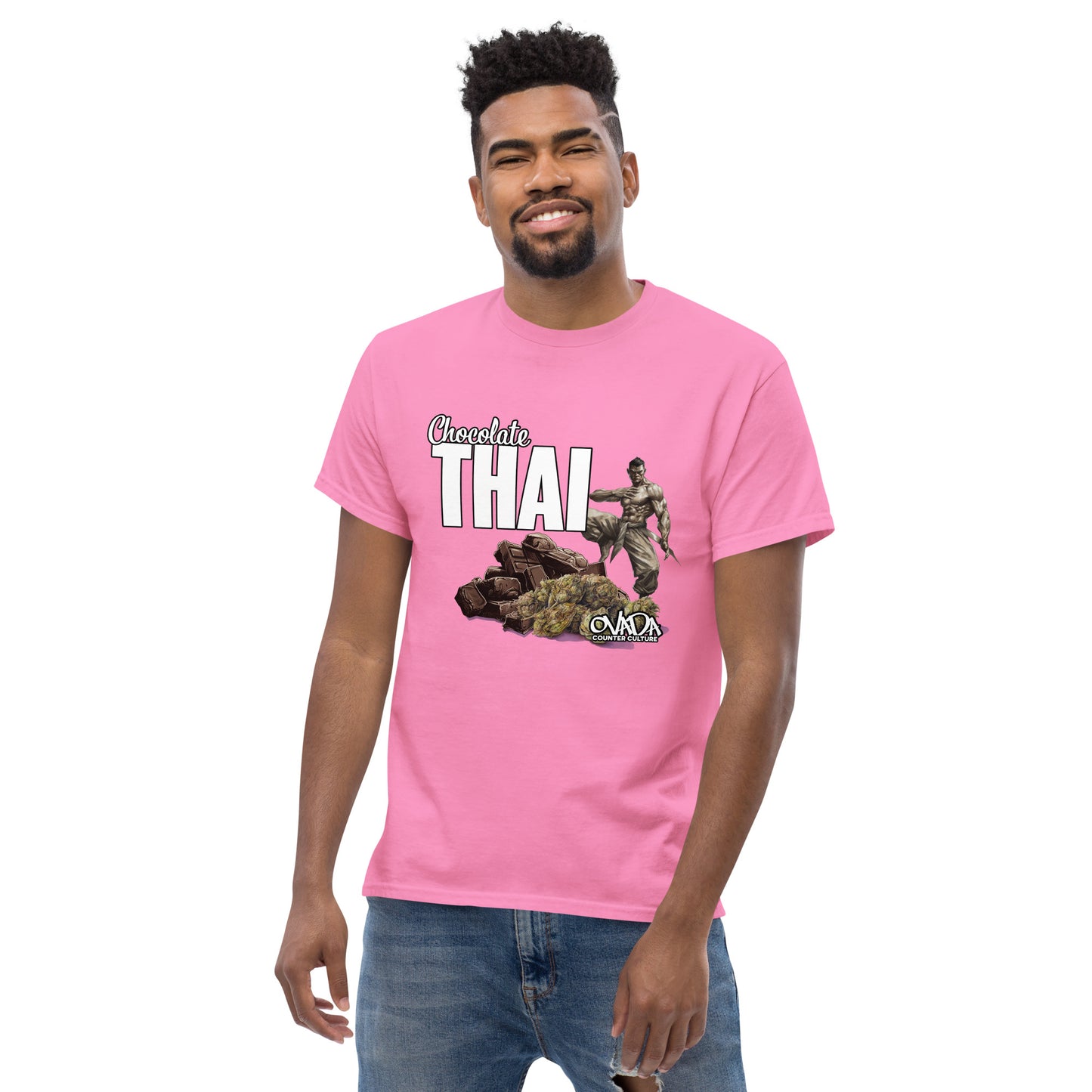 A man in a pink cotton graphic t-shirt with the words Chocolate Thai. A cartoon depiction of a Muay Thai Fighter is standing on a pile of chocolates, with marijuana buds in front of it.
