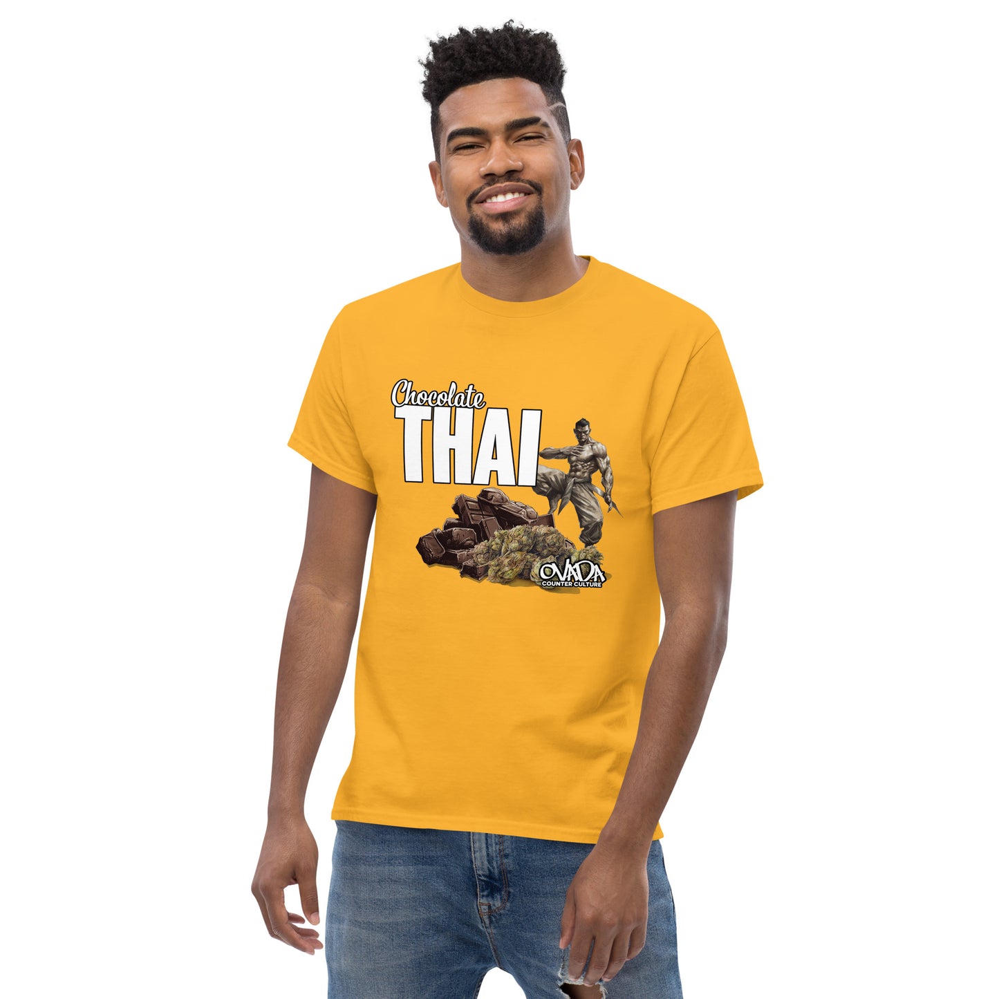 A man in a gold yellow cotton graphic t-shirt with the words Chocolate Thai. A cartoon depiction of a Muay Thai Fighter is standing on a pile of chocolates, with marijuana buds in front of it.