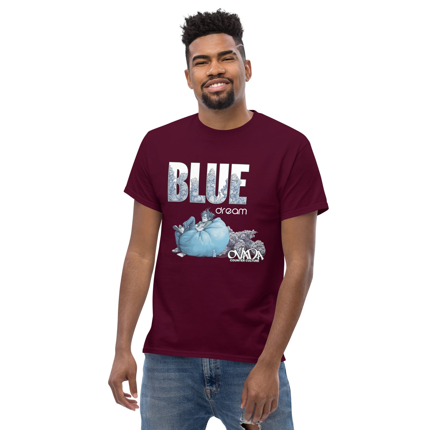 A man in a maroon cotton graphic t-shirt with the words Blue Dream. A monochromatic blue cartoon depiction of a stoner passed out in a bean back with marijuana buds behind him. Weed