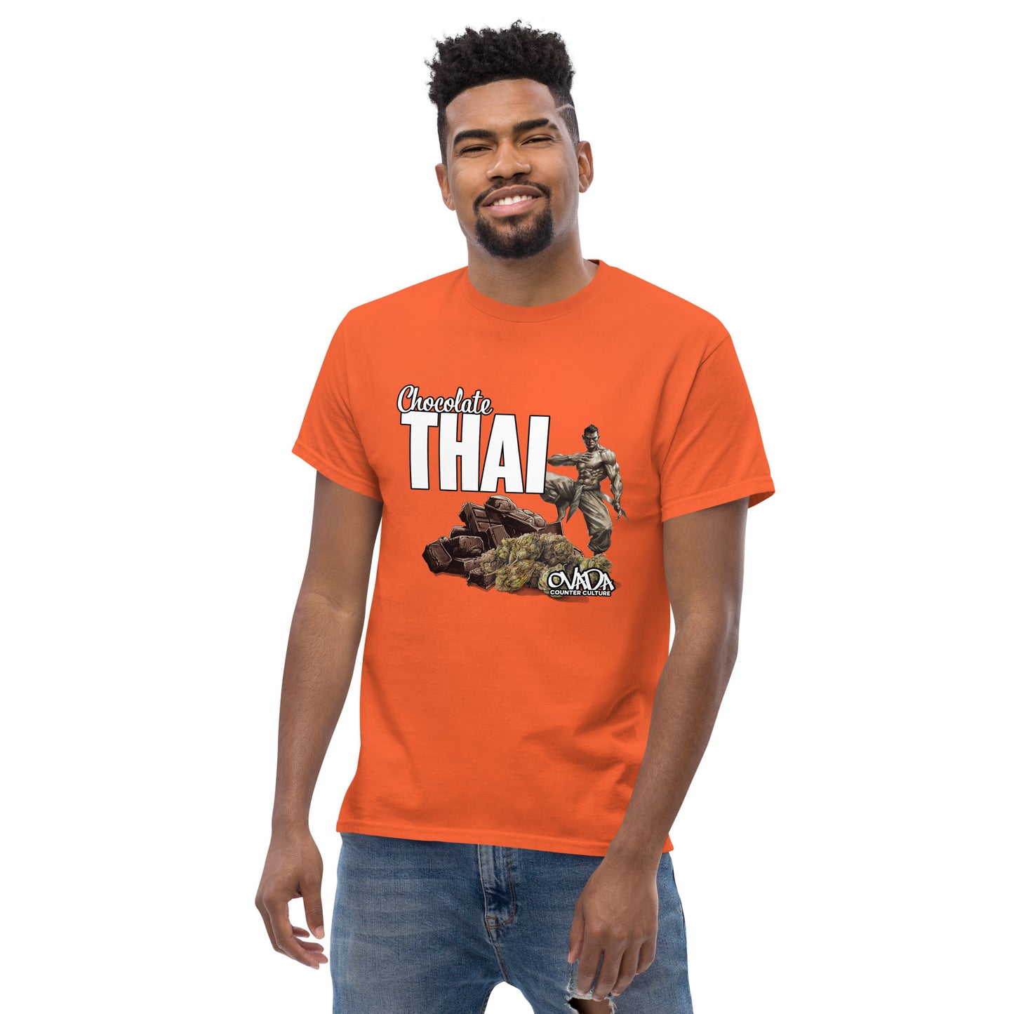 A man in an orange cotton graphic t-shirt with the words Chocolate Thai. A cartoon depiction of a Muay Thai Fighter is standing on a pile of chocolates, with marijuana buds in front of it. 